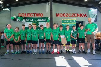 Grupa młodych piłkarzy w zielonych strojach klubowych pozująca do pamiątkowego zdjęcia z trenerem po odebraniu medali