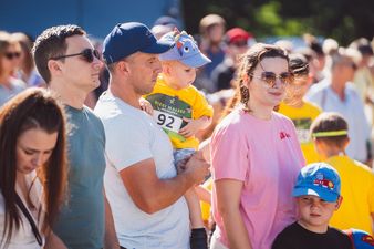 Mężczyzna trzyma dziecko na rękach, obok kobieta w różowej koszulce wraz z małym chłopcem u boku