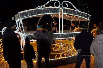 Ludzie oglądający z bliska dużą instalację świąteczną w kształcie karety, rozświetloną białym i żółtym światłem LED