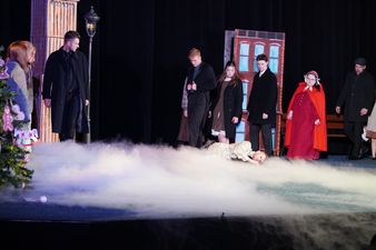 Scena w której aktorzy patrzą na leżącego głównego bohatera, po scenie snuje się dym.