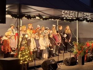 Dzieci w przebraniach aniołów i królów występują na scenie pod udekorowanym świątecznie namiotem „Sołectwo Bzie”
