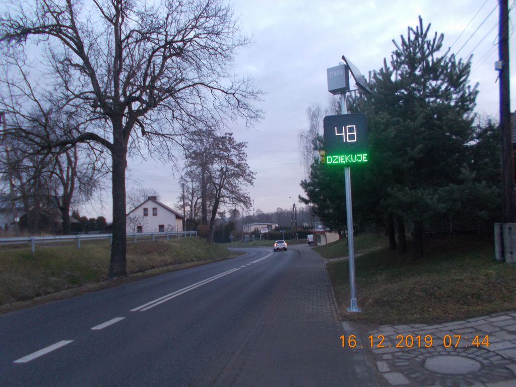 Tablca elektroniczna do mierzenia prędkości przy ulic, w oddali samochód, przystanek i domy