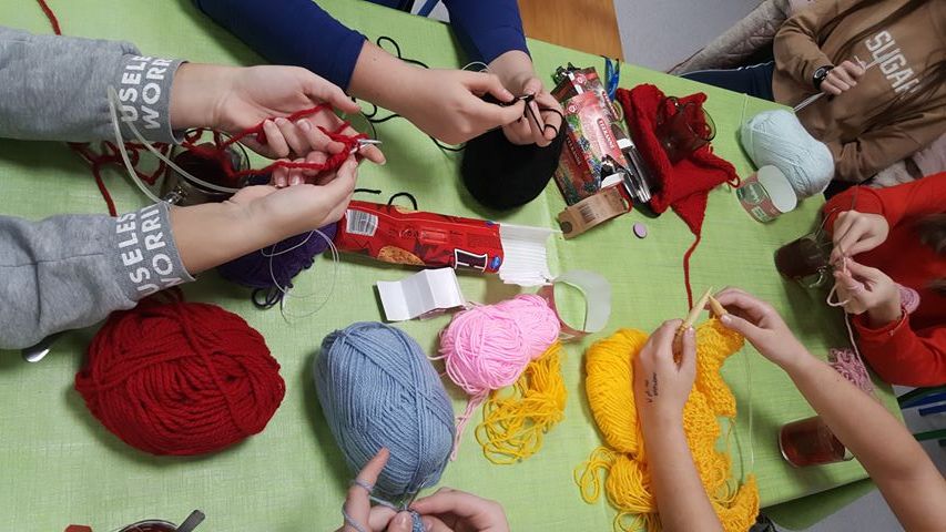 Dłonie dzieci, dziergających z włóczki szaliki w różnych kolorach żółty, czerwony, niebieski, różowy, czarny