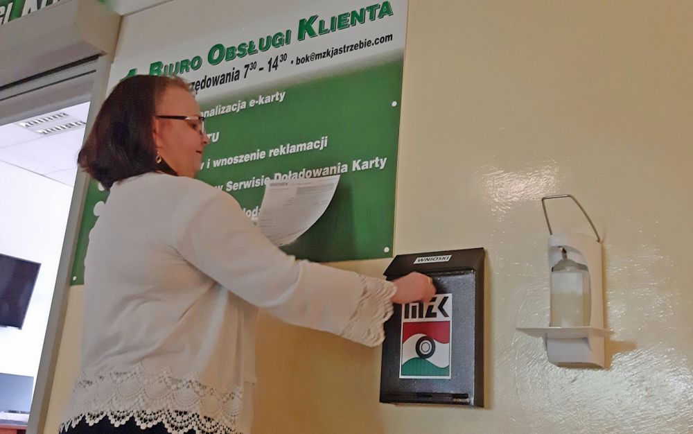 Kobieta wrzucająca kartkę do skrytki MZK