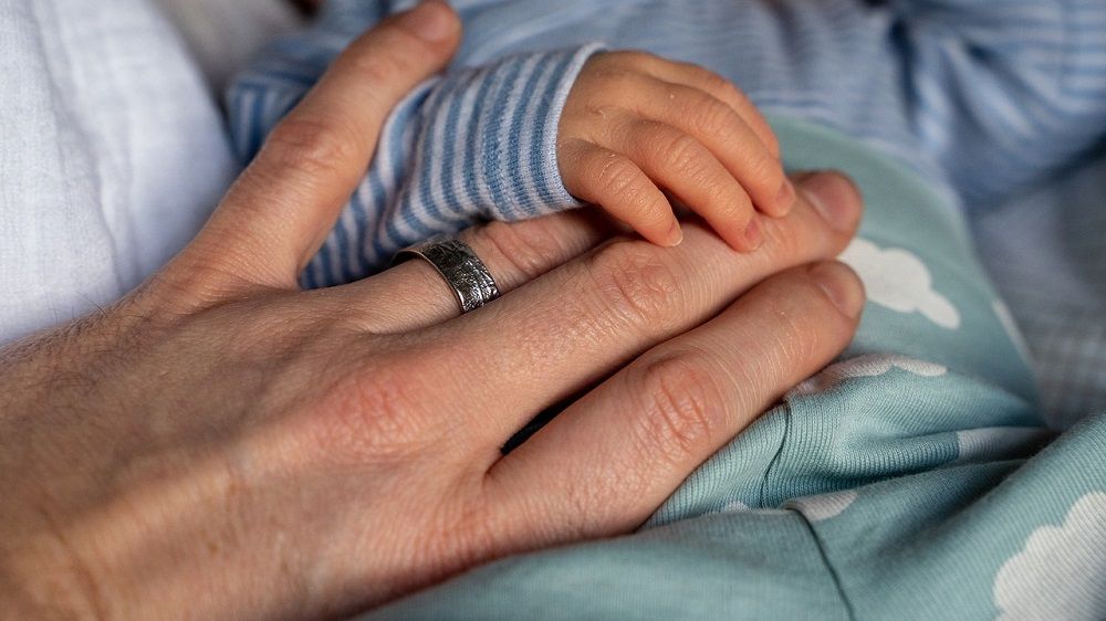 Na zdjęciu widoczne są dłonie dorosłego mężczyzny i noworodka.