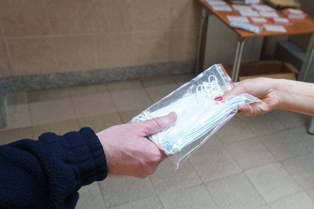 Na zdjęciu widać przekazanie paczki maseczek prez jedną osobę drugiej 