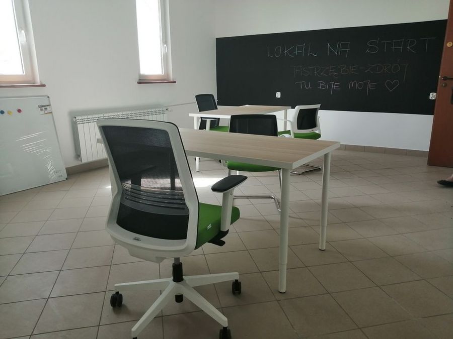 Wnętrze lokalu na start: biurko z krzesłem biurowym, w tle tablica z napisem "lokal na start"