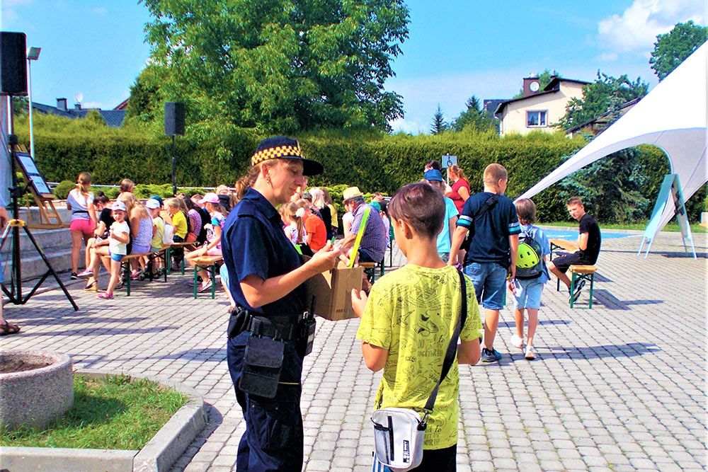 Zdjęcie strażniczki rozdającej odblaski - w tle bawiące się dzieci.