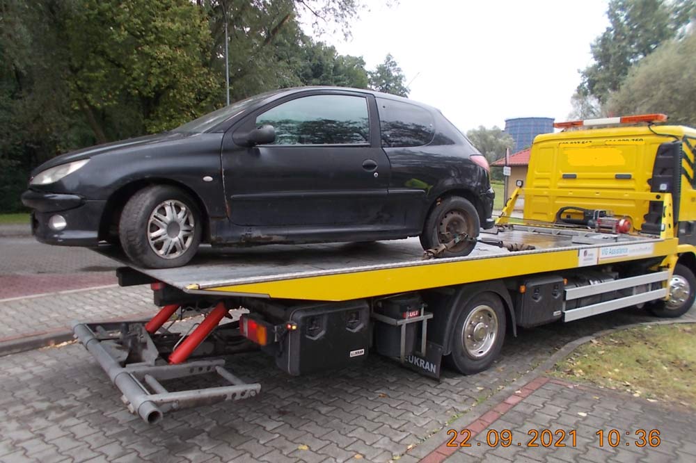 Zdjęcie przedstawia wrak czarnego auta na lawecie.