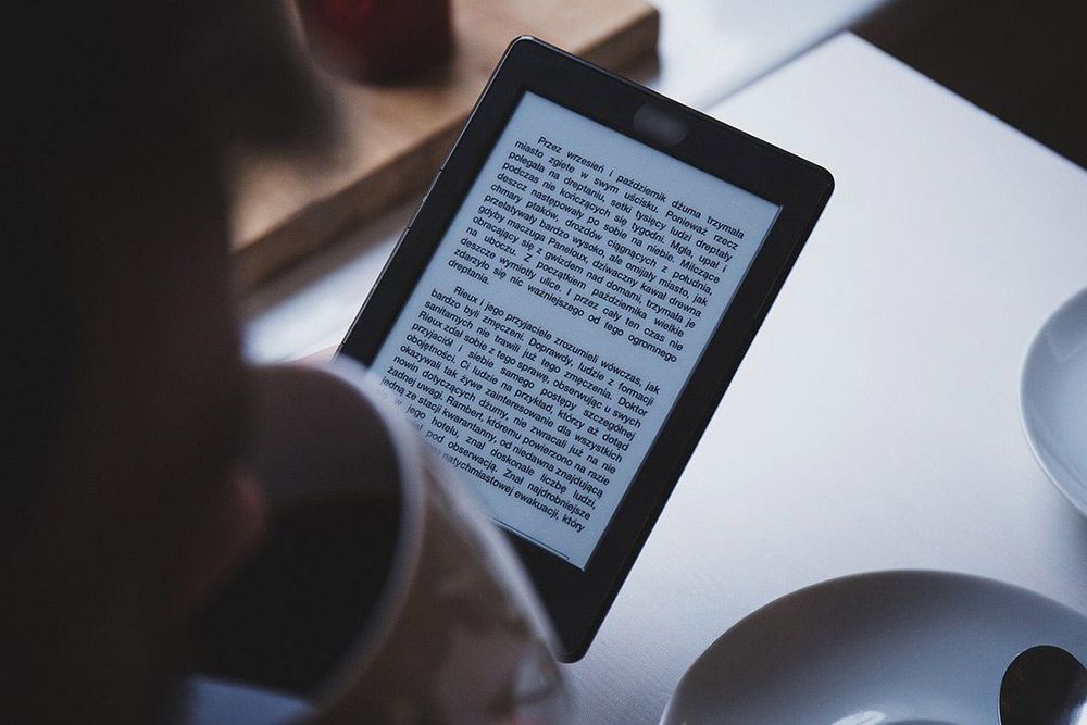 Zdjęcie przedstawia osobę czytającą książkę przy pomocy czytnika ebook.