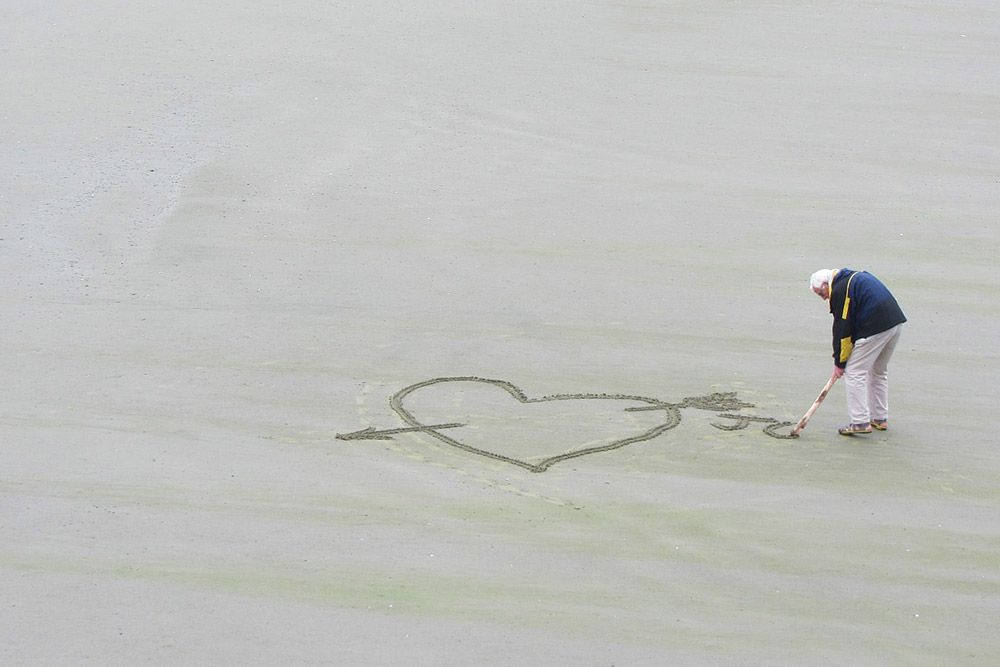 Senior rysuje na piasku serce.