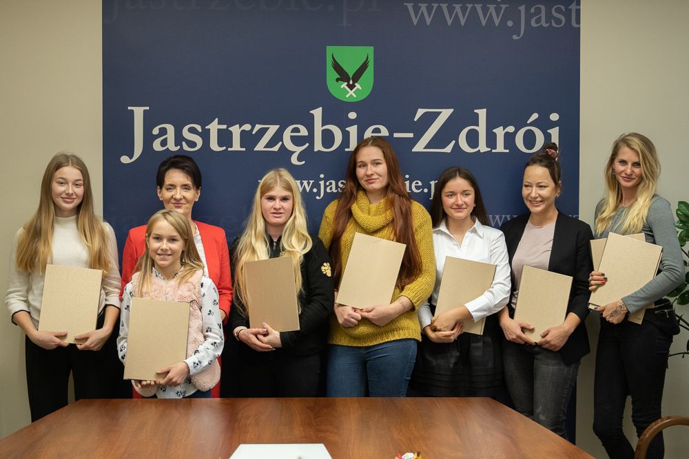Uczestniczki spotkania pozują do wspólnego zdjęcia z Anną Hetman. W tle ścianka z napisem "Jastrzębie-Zdrój" i herbem miasta.