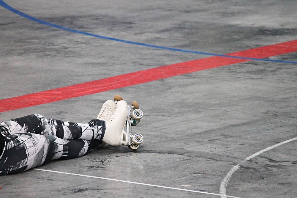 Zdjęcie przedstawia osobę na wrotkach na płycie boiska.