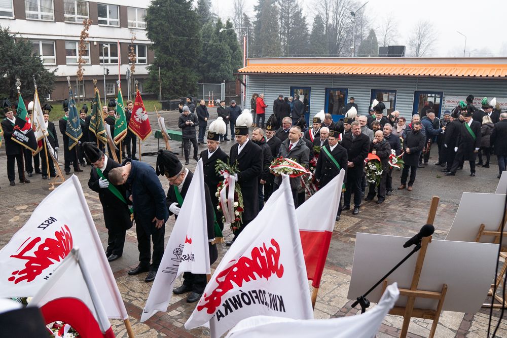 Uczestnicy uroczystości składają kwiaty pod tablicą pamiątkową.