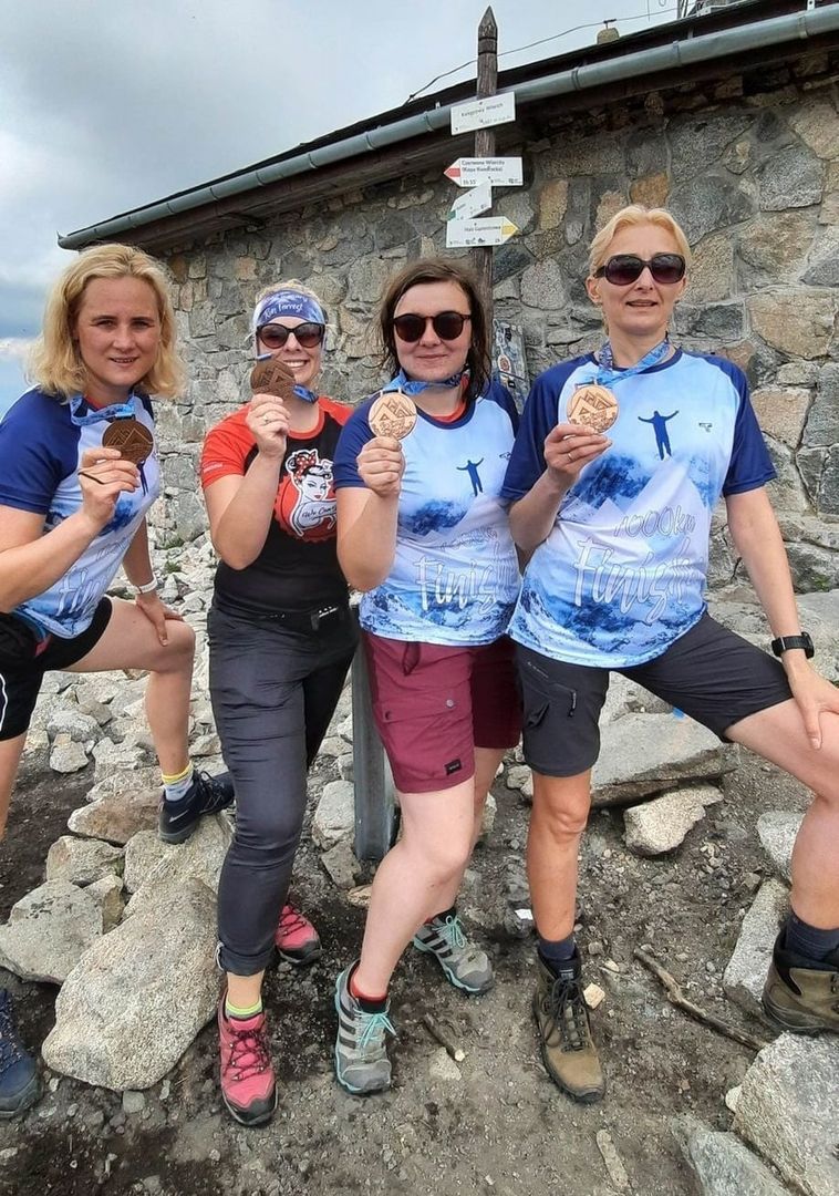 4 zawodniczki na szczycie góry, pokazują medale