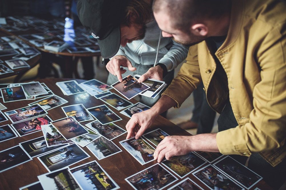 mężczyźni pochylają się nad leżącymi na stole fotografiami