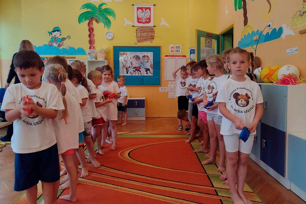 Dzieci stoją w dwóch rzędach, mają sportowe stroje.