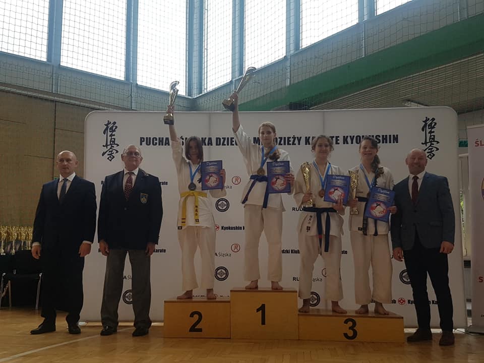 Medaliści stojący na podium, obok oficjele