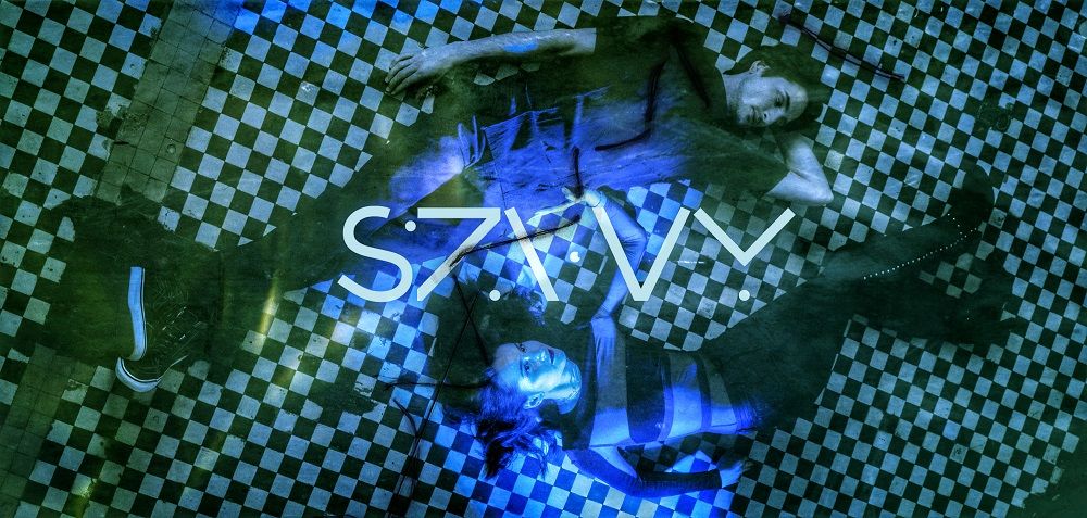 dwie osoby leżą na podłodze, niebieski neon "SZWY"