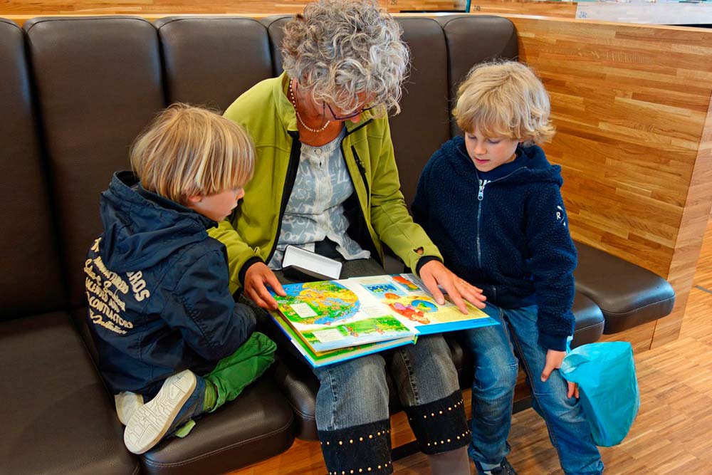 Zdjęcie przedstawia osobę czytającą dzieciom książkę.