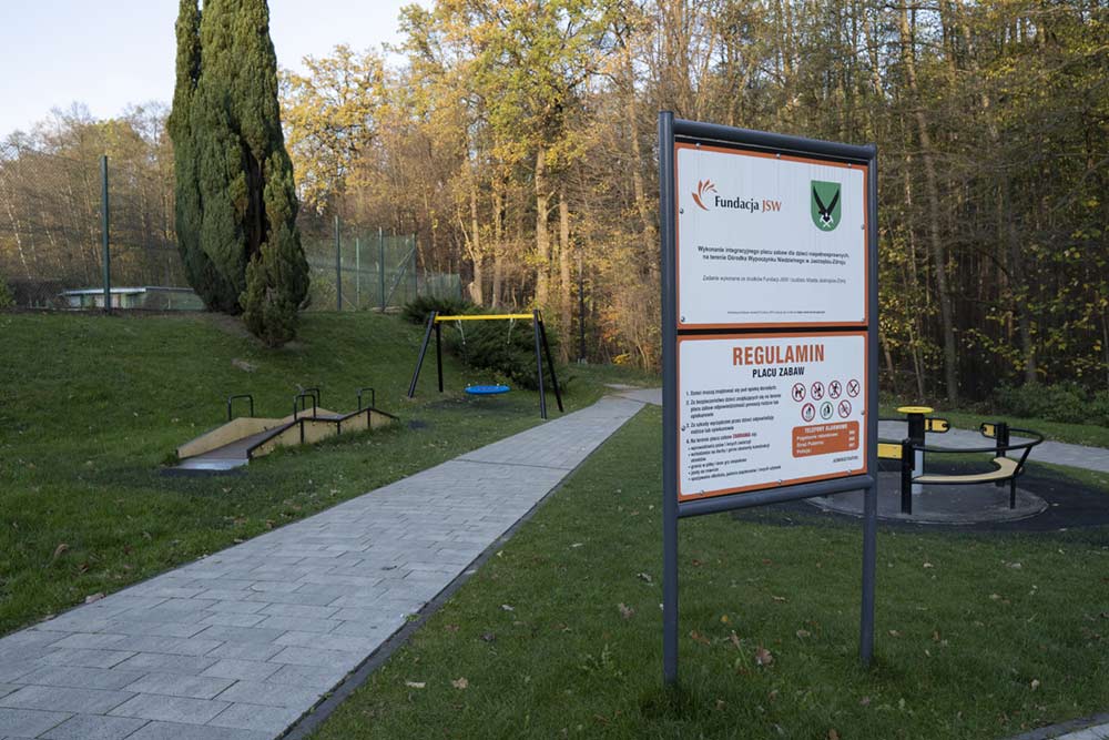 Widok na plac integracyjny i tablicę z regulaminem i herbem miasta oraz logo Fundacji JSW.