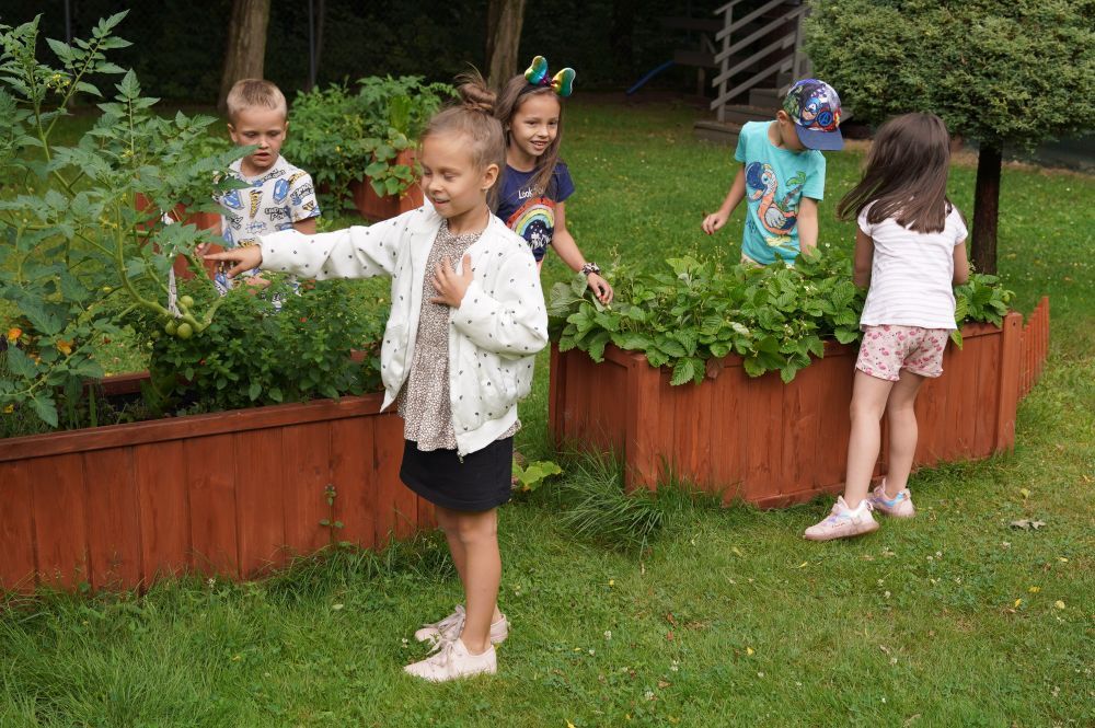 Zdjęcie przedstawia dzieci przedszkolne podczas zabawy w ogrodzie.