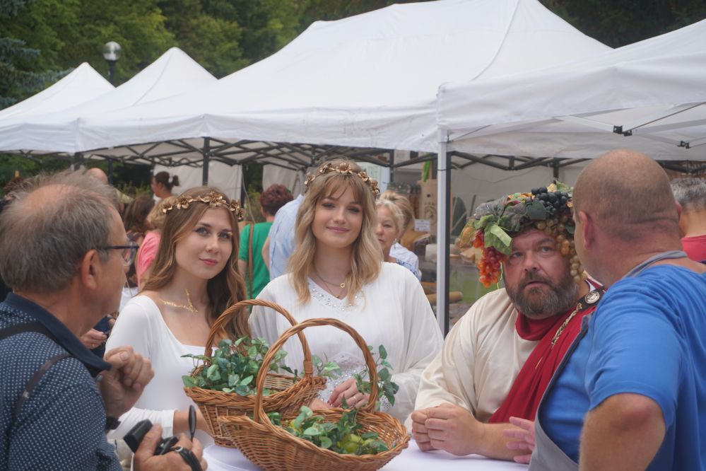 Mężczyzna przebrany za boga wina z dwoma kobietami ubranymi w stylu starożytnej Grecji rozmawiającymi z mieszkańcami