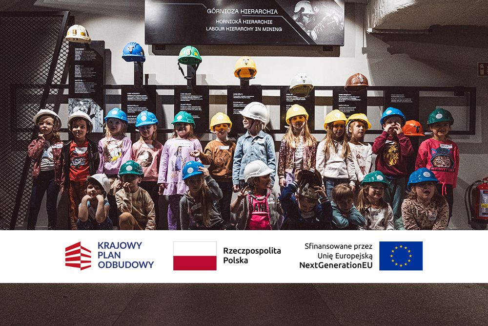 Grupa dzieci w kaskach górniczych w różnych kolorach. Ponizej zdjęcia znajduja się logotypy: Krajowy Plan Odbudowy, flaga Rzeczpospolitej Polski, flaga Unii Europejskiej z dopiskiem sfinansowane przez Unię Europejską, NextGenerationEU