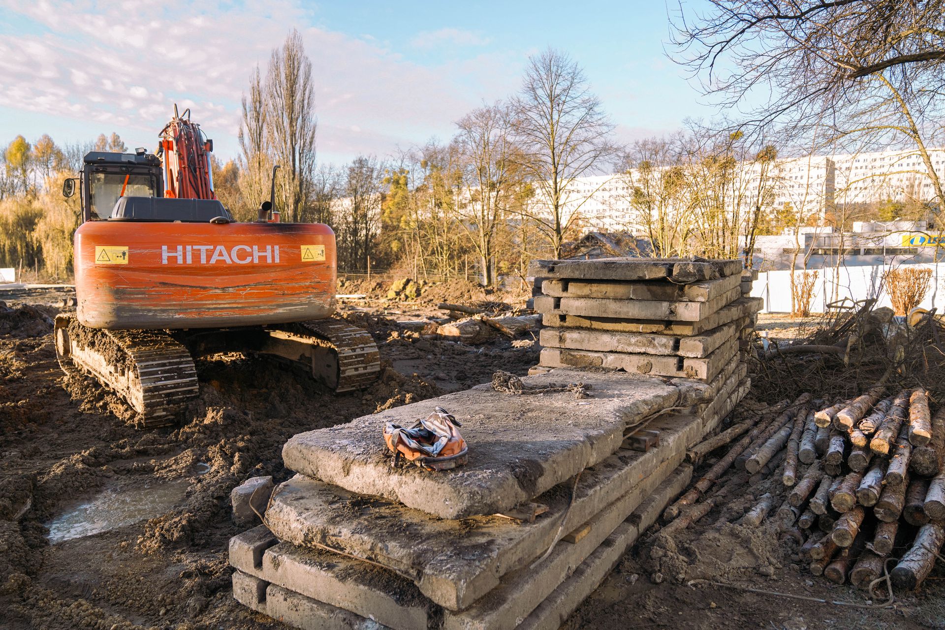 Dźwig Hitachi i kostka betonowa z plami drzew na placu budowy