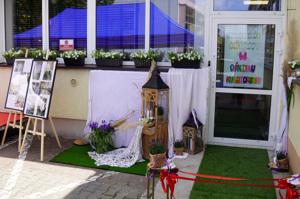 Otwarcie ośrodka kuratorskiego - rozciągnięta wstęga przed drzwiami z napisem serdecznie witamy w ośrodku kuratorskim