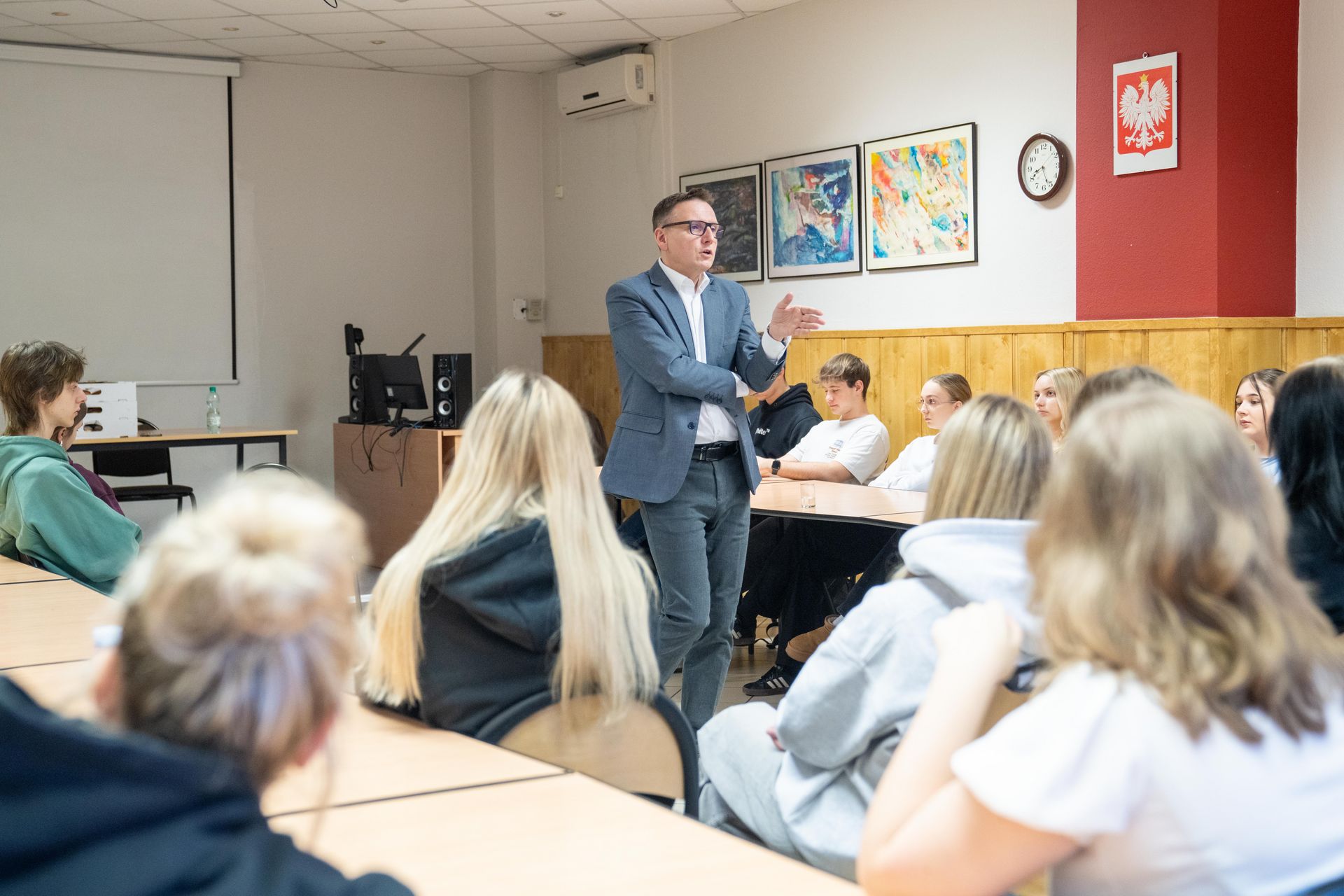 Uczniowe siedzący w klasie, prezydent jednej z uczennic wręcza upominek