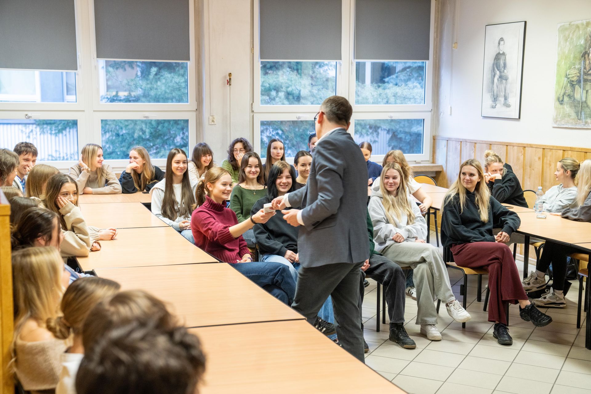 Uczniowie siedzący w klasie, prezydent jednej z uczennic wręcza upominek