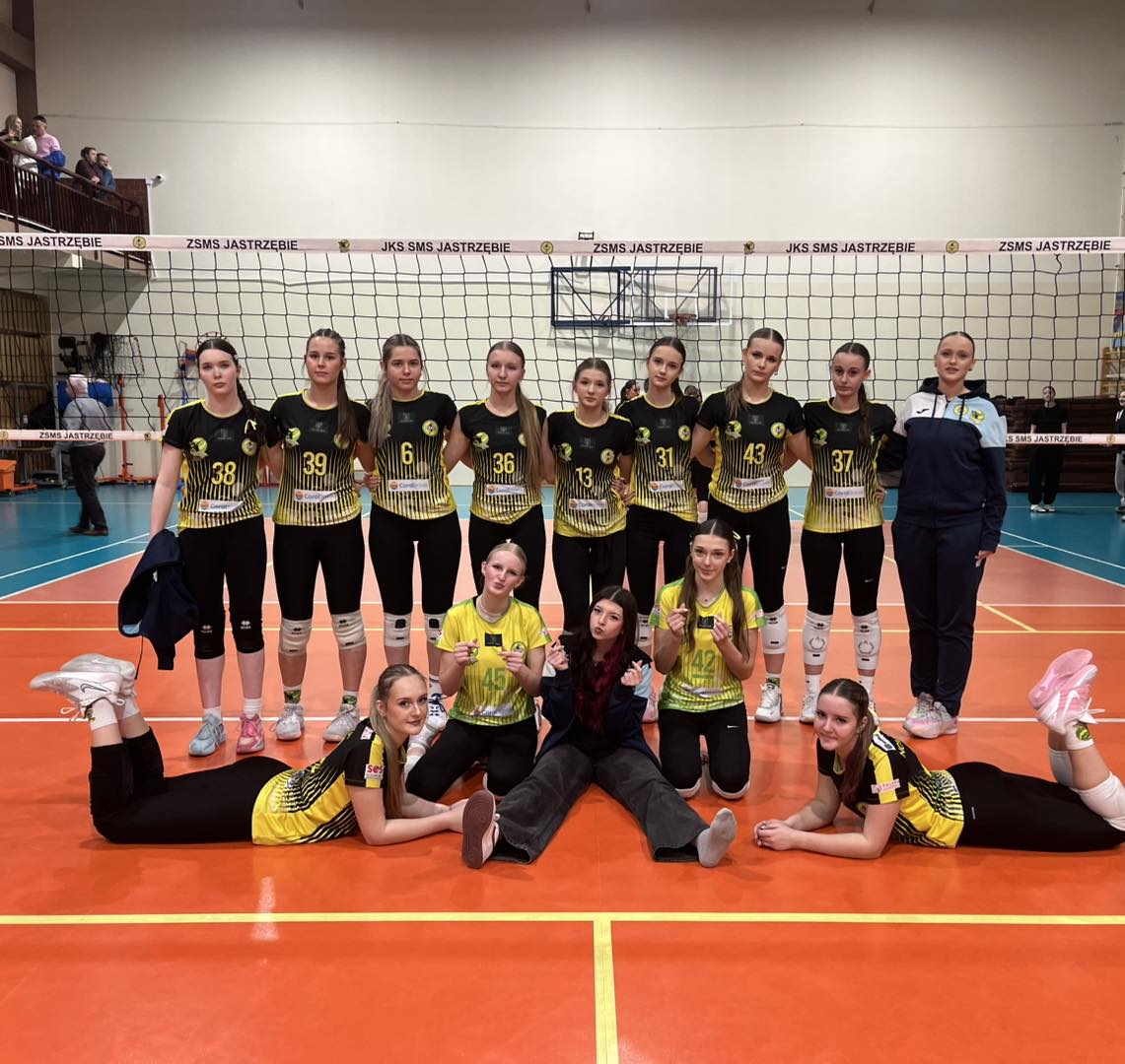 drużyna juniorek młodszych w dwóch szeregach - jeden stojący wzdłurz siatki, drugi klecząco-leżący przed pierwszym