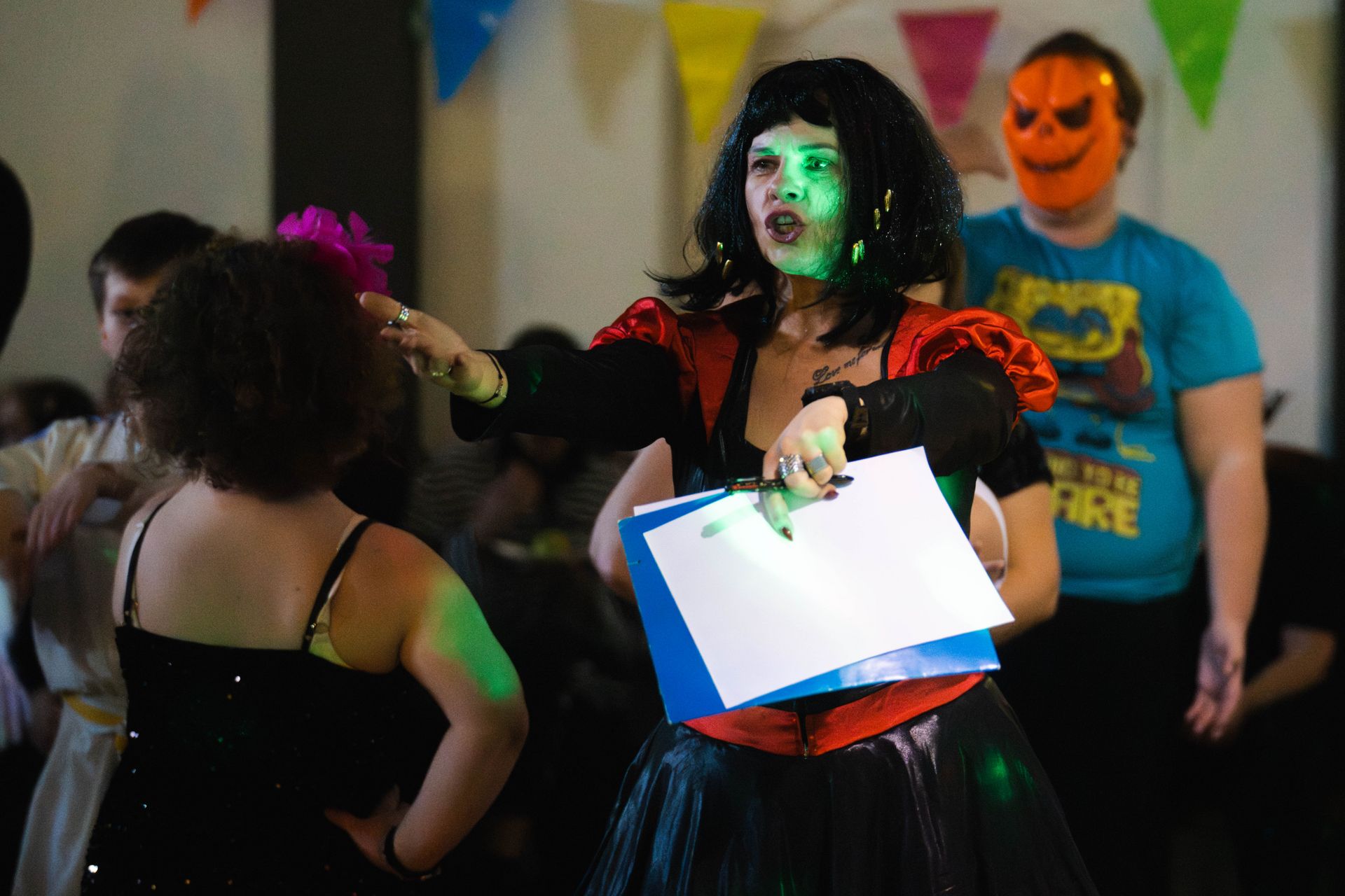 trzy osoby bawią się jedna ma pomarńczową maskę na twarzy, druga pomalowana twarz na biało, trzecia jest odwrócona tyłem