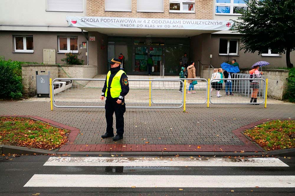 Strażnik przy przejściu dla pieszych, w tle szkoła.